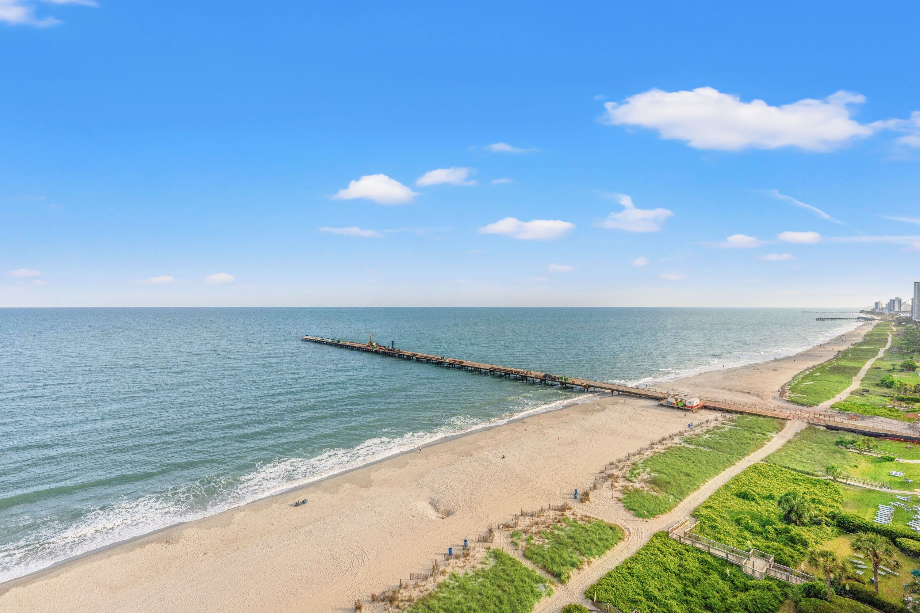 Une plage côtière avec une jetée qui s’avance dans la mer, un rivage sablonneux et un ciel dégagé.