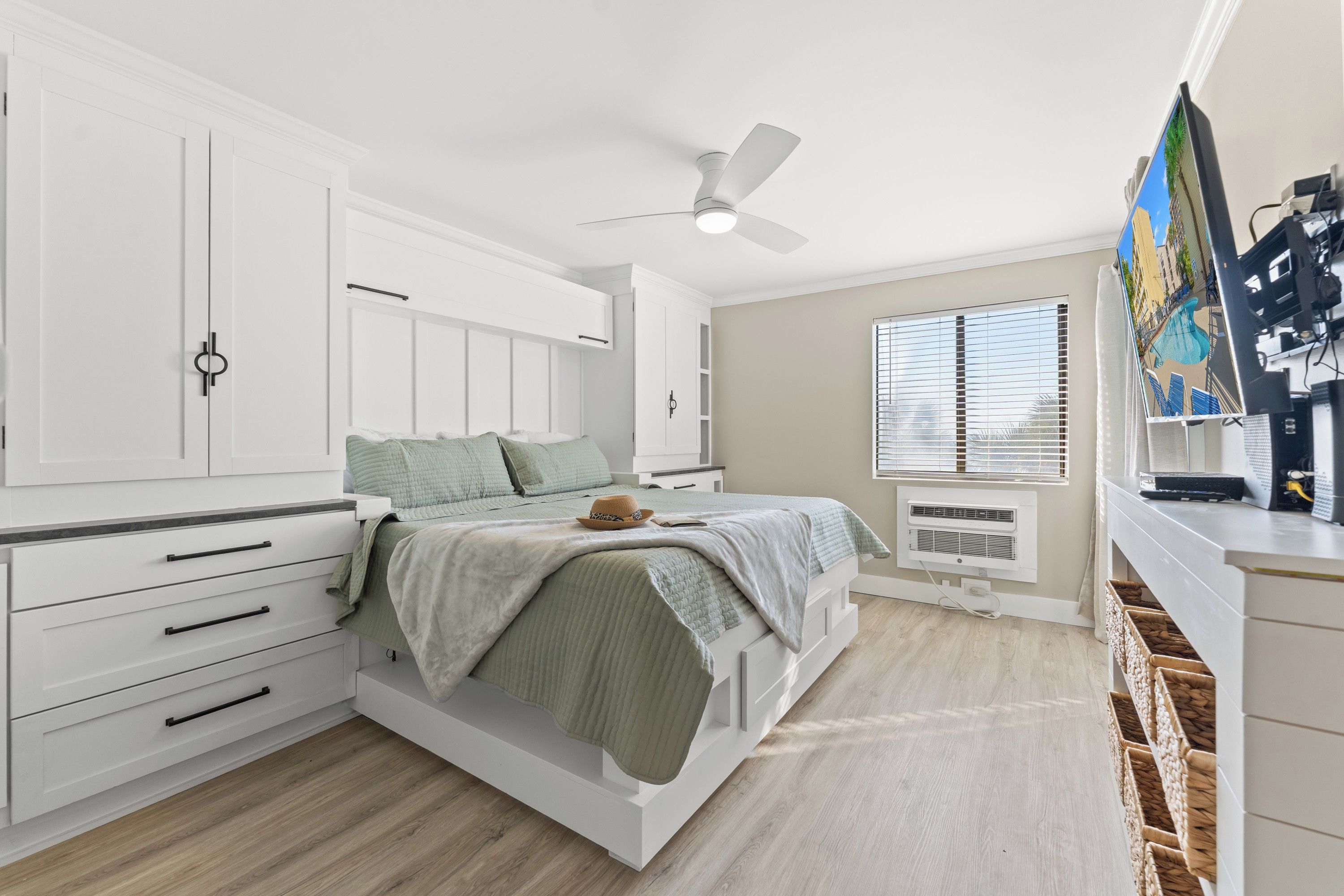 A bedroom with a bed, white wardrobe, ceiling fan, window with blinds, and a wall-mounted air conditioner.