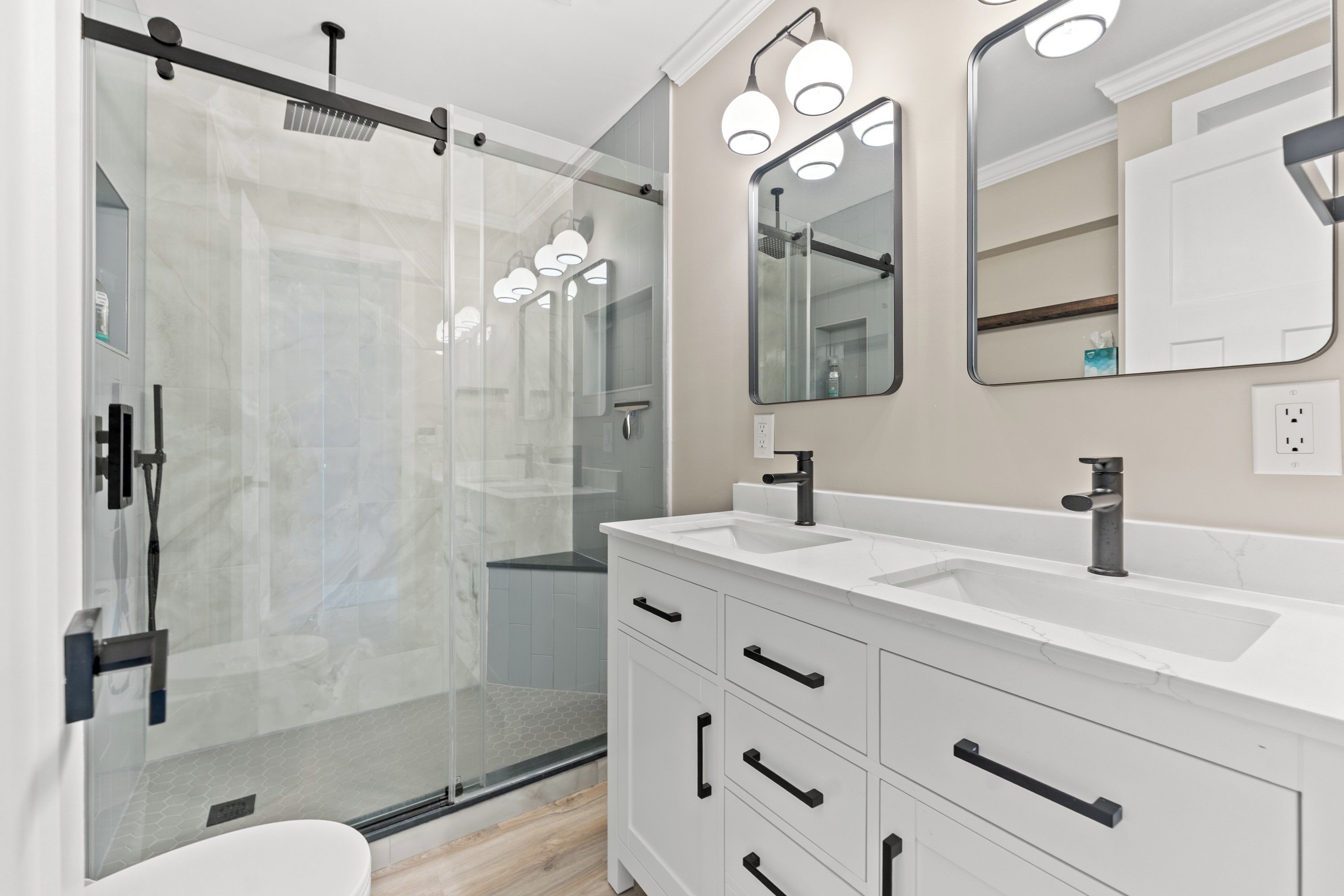 Un baño moderno con cabina de ducha de vidrio, tocador blanco con pomos negros y un espejo grande.