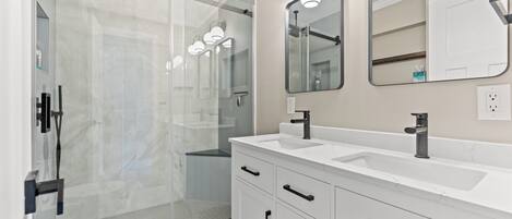 A modern bathroom with a glass shower enclosure, a white vanity with black handles, and a large mirror.