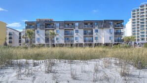 A multi-story residential building with balconies, located near a sandy beach area. - Long Bay Dunes by Elliott Beach Rentals (Myrtle Beach)