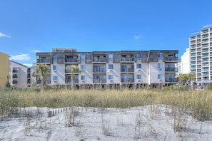 A multi-story residential building with balconies, located near a sandy beach area.