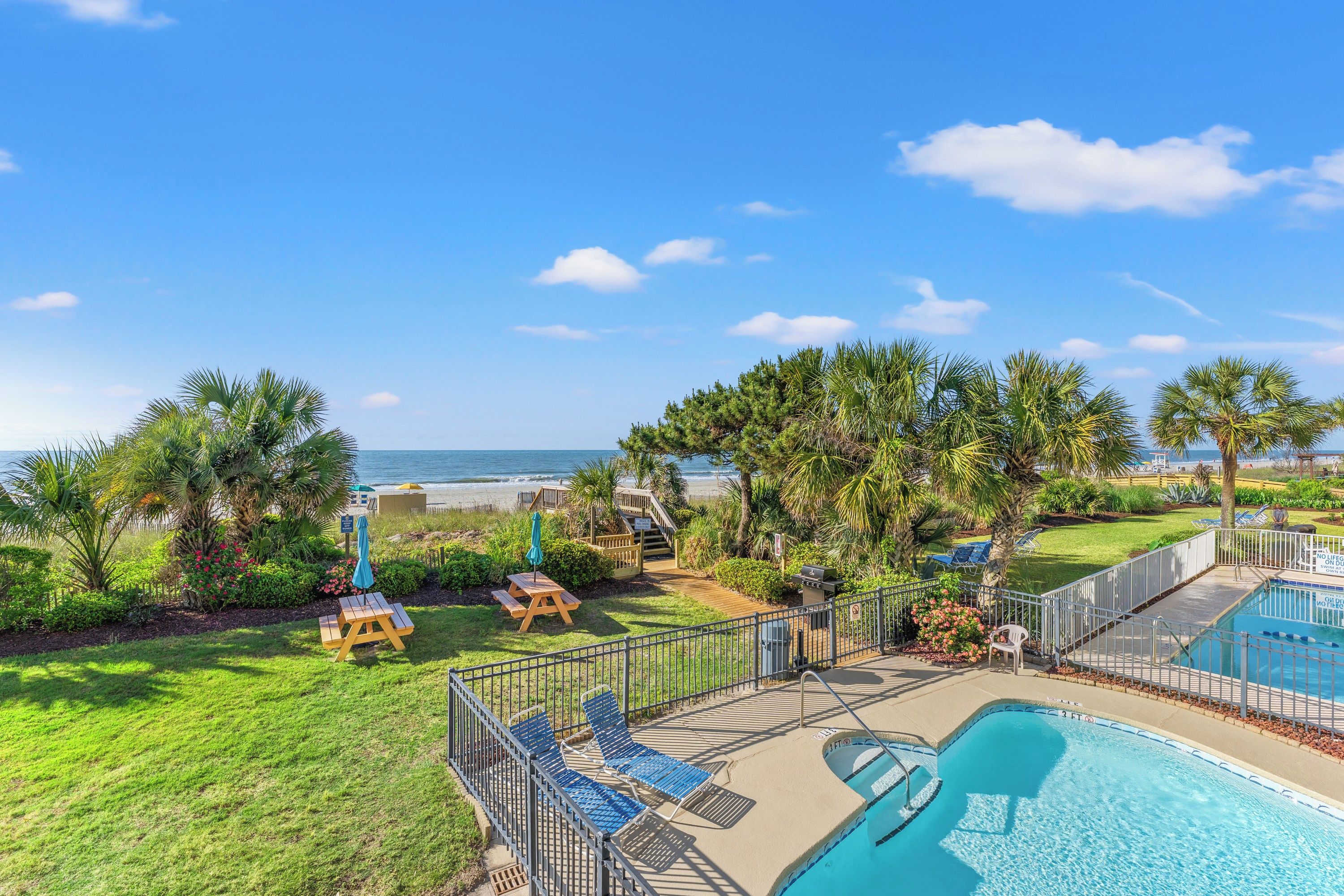 A pool area with a view of the ocean, surrounded by palm trees and a wooden deck.