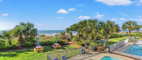 A pool area with a view of the ocean, surrounded by palm trees and a wooden deck.