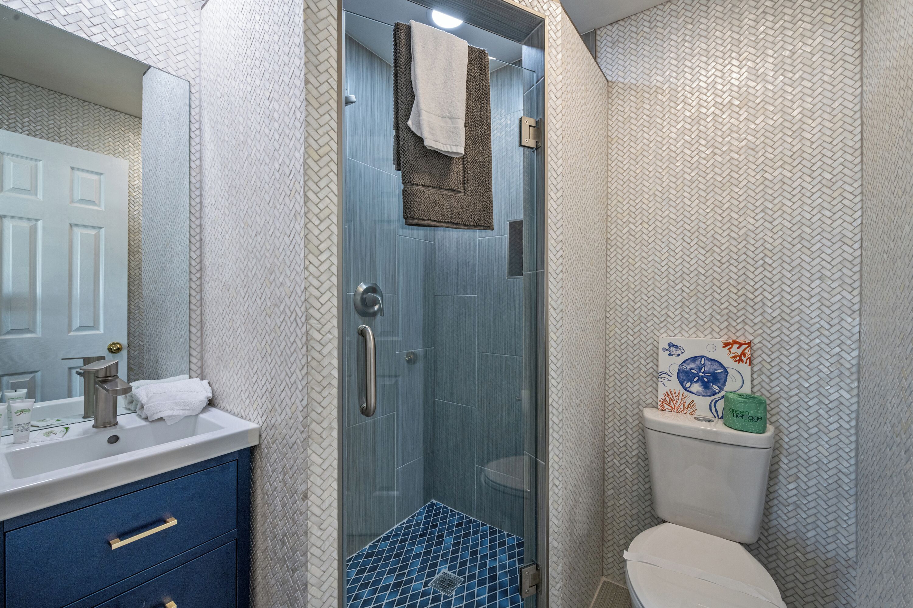 Un baño con cabina de ducha de vidrio, un inodoro blanco y suelo de ducha con azulejos azules.