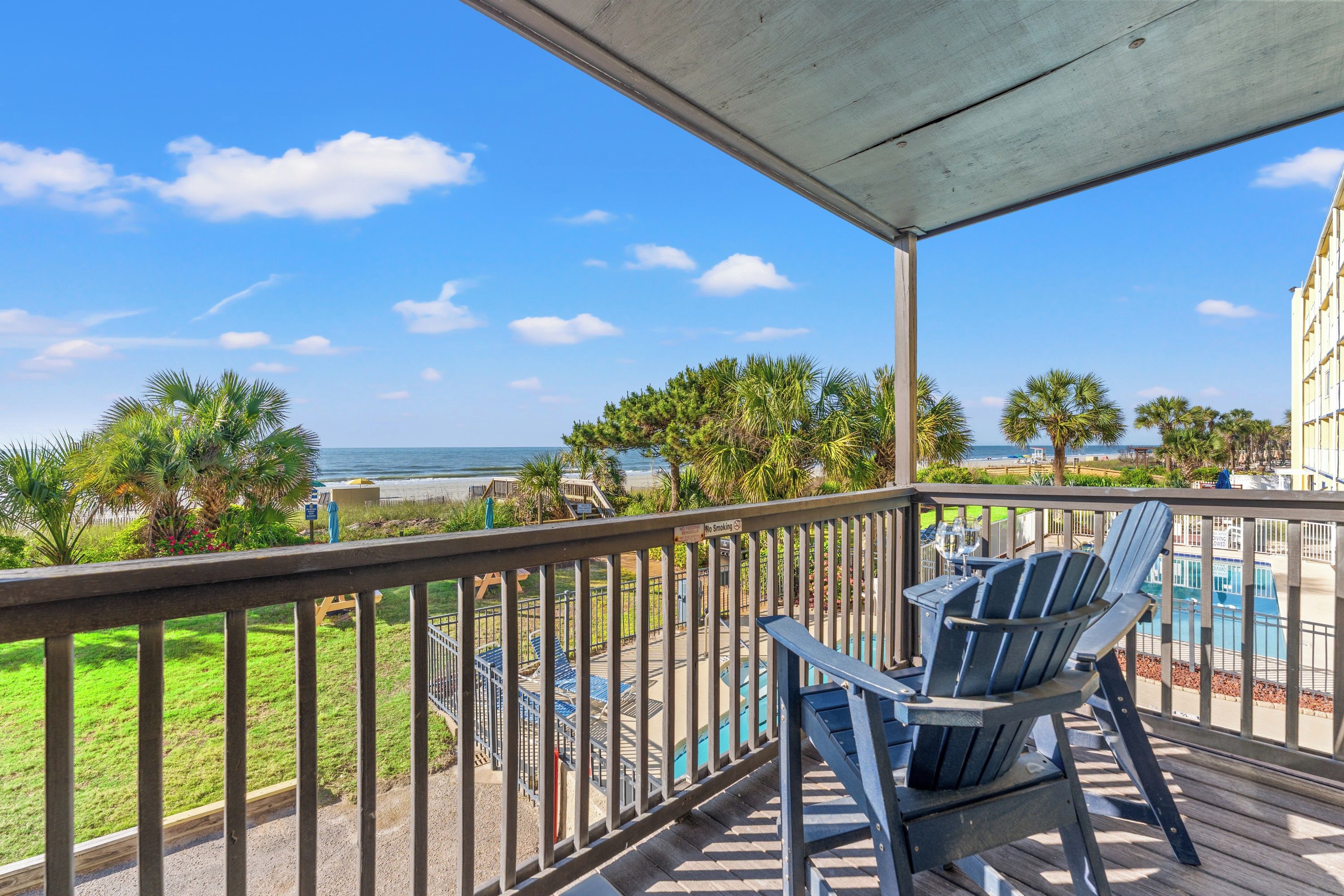 A balcony with a view of the ocean, outdoor seating, and a pool area.