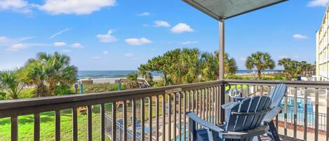 A balcony with a view of the ocean, outdoor seating, and a pool area.