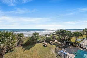 A pool area with a view of the beach, palm trees, and a deck with lounge chairs. - Long Bay Dunes by Elliott Beach Rentals (Myrtle Beach)