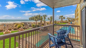 A balcony with a view of the beach and ocean, a pool, and outdoor seating.