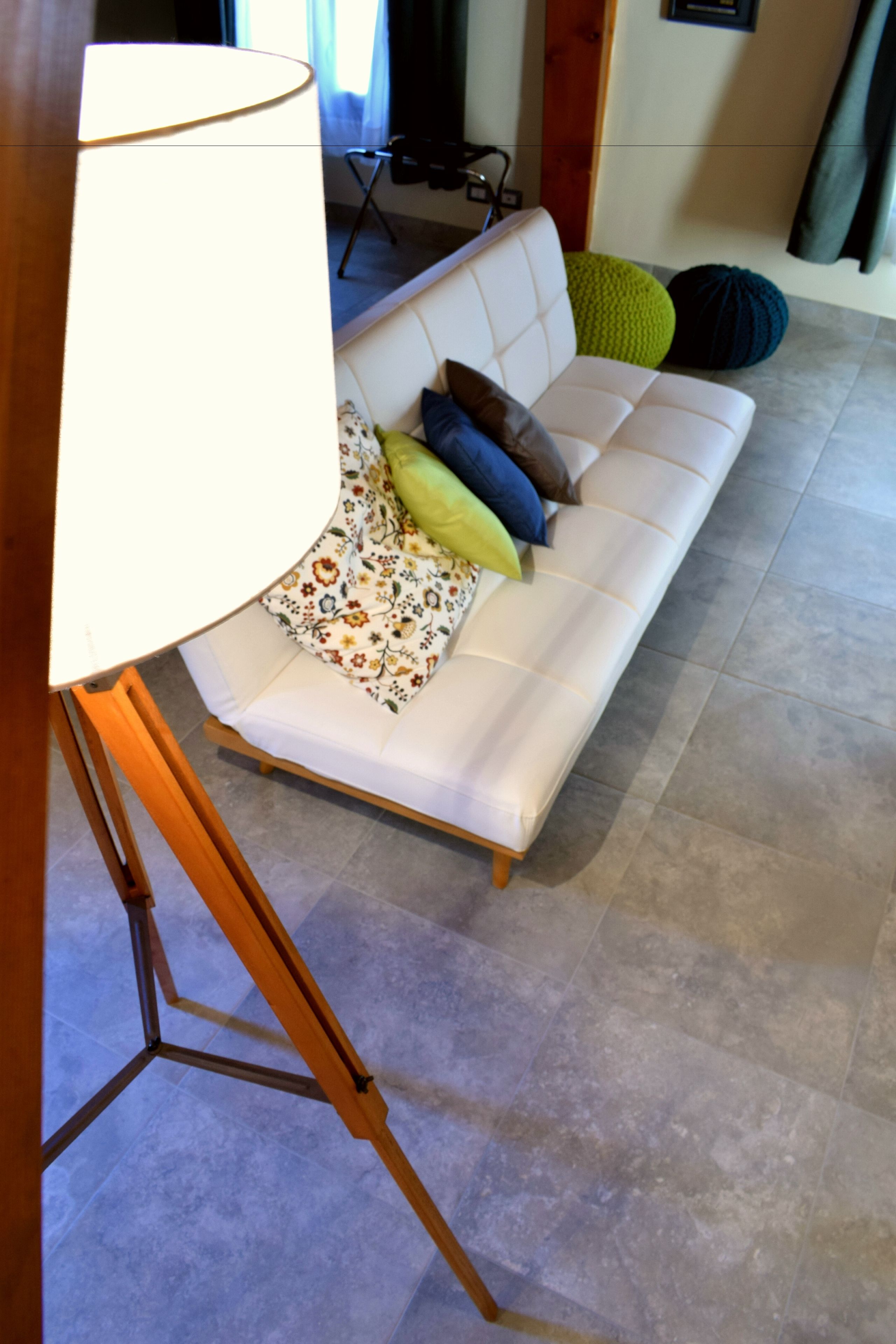 A white sofa with colorful cushions, a wooden floor lamp, and a patterned throw.