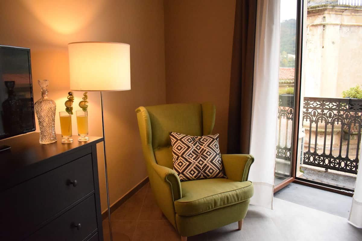 A green armchair with a patterned cushion, a floor lamp, and a television on a black cabinet.