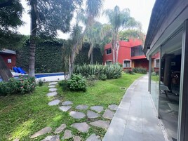 Un jardín con un sendero de piedra, palmeras y un edificio rojo con puerta de vidrio.