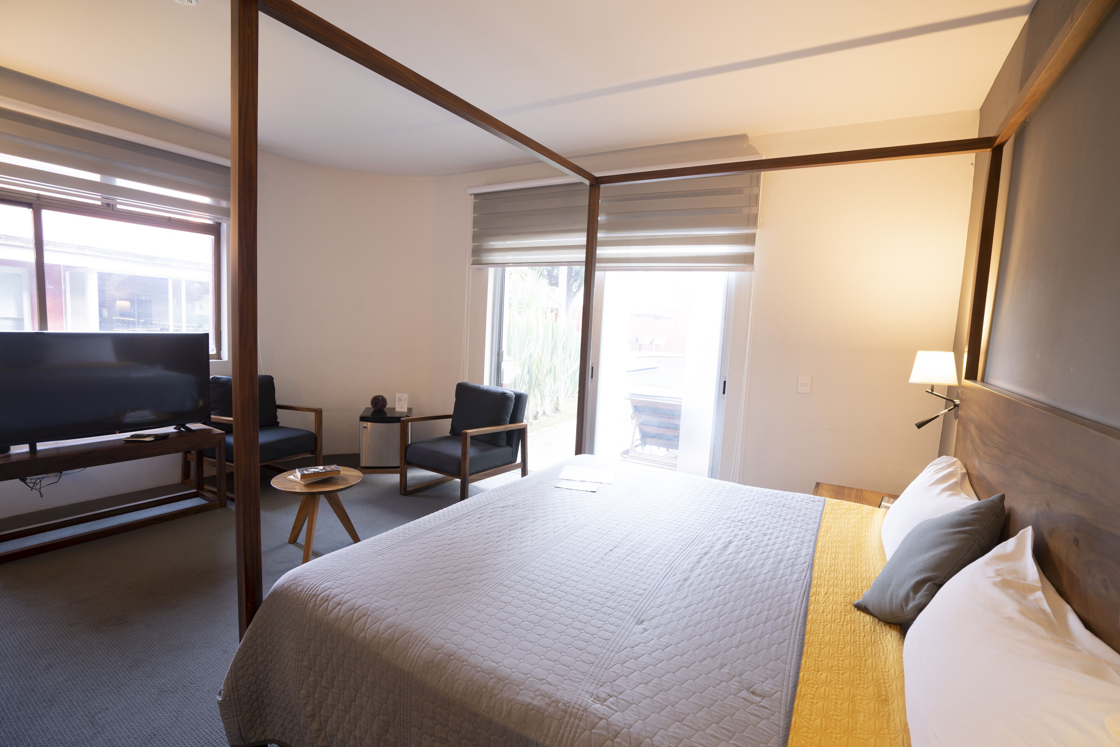 A hotel room with a four-poster bed, a TV, a desk with a chair, and a window with blinds.