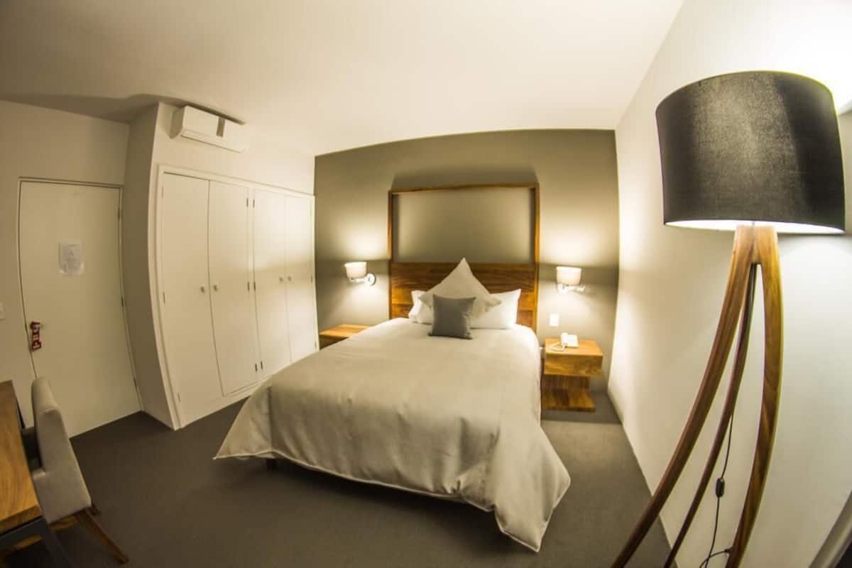 Una habitación de hotel con una cama grande, un armario, lámparas de noche y una lámpara de pie.