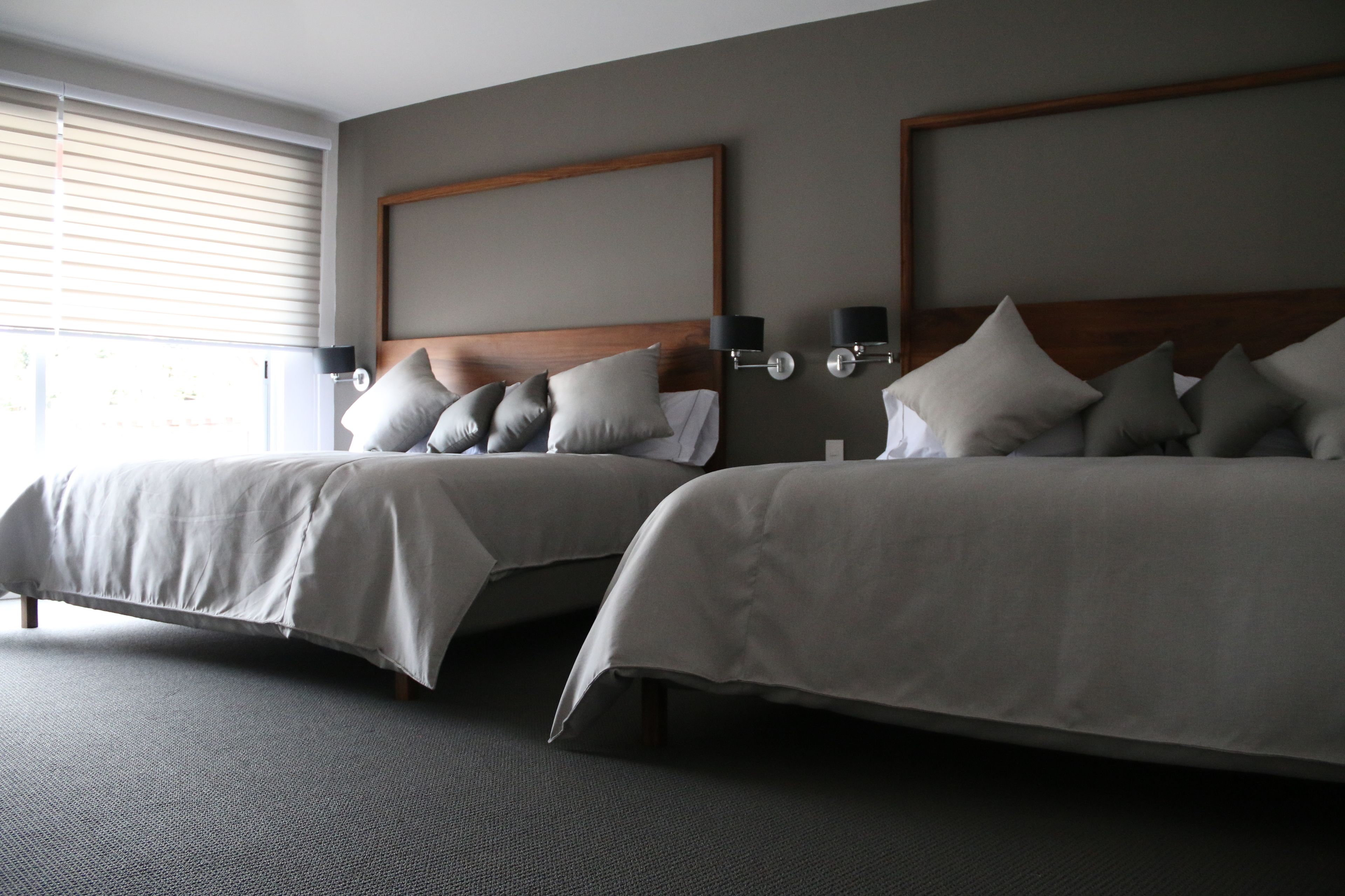 A hotel room with two beds, a large window with blinds, and a neutral color scheme.