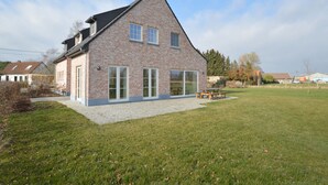 A modern brick house with a sloped roof, large glass windows, and a paved patio area. - Sint-Amands Country Escape (Sint Amands)