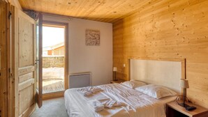 A wooden-paneled bedroom with a bed, a nightstand, a lamp, and a view of the outside. - Apartment in Flaine with Ski Lift Access (Arâches-La-Frasse)