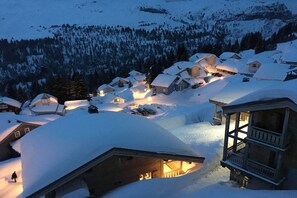 A snow-covered village with wooden houses, a wooden structure with a balcony, and a lit interior.
