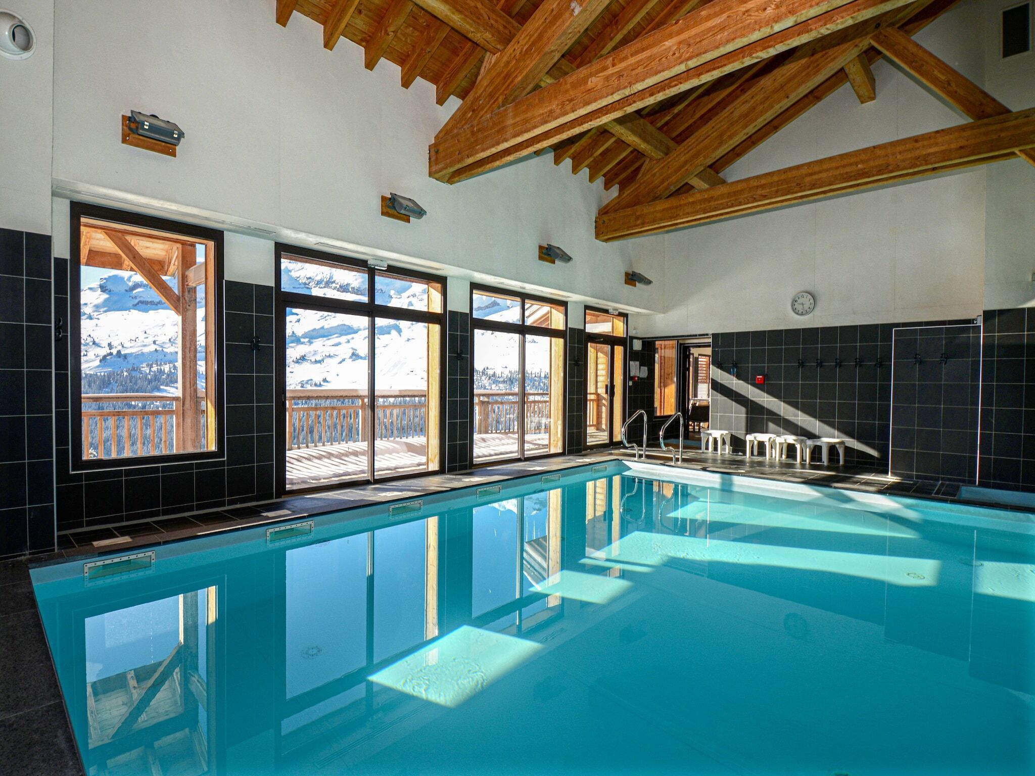 A swimming pool with a view of snow-capped mountains through large windows.
