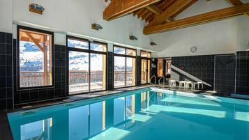A swimming pool with a view of snow-capped mountains through large windows.