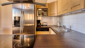 A modern kitchen with stainless steel appliances, wooden cabinets, and a sleek countertop. - Grand Massif Family Retreat (Arâches-La-Frasse)