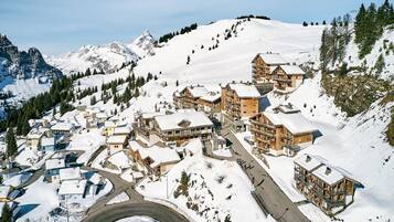 Un village de montagne enneigé, avec des bâtiments en bois, une route sinueuse et une vue dégagée sur les sommets environnants.