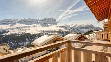A wooden cabin with a wooden deck overlooking a snowy mountain landscape.