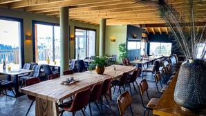 A restaurant with wooden tables and chairs, large windows, and a peacock feather decoration. - Grand Massif Family Retreat (Arâches-La-Frasse)