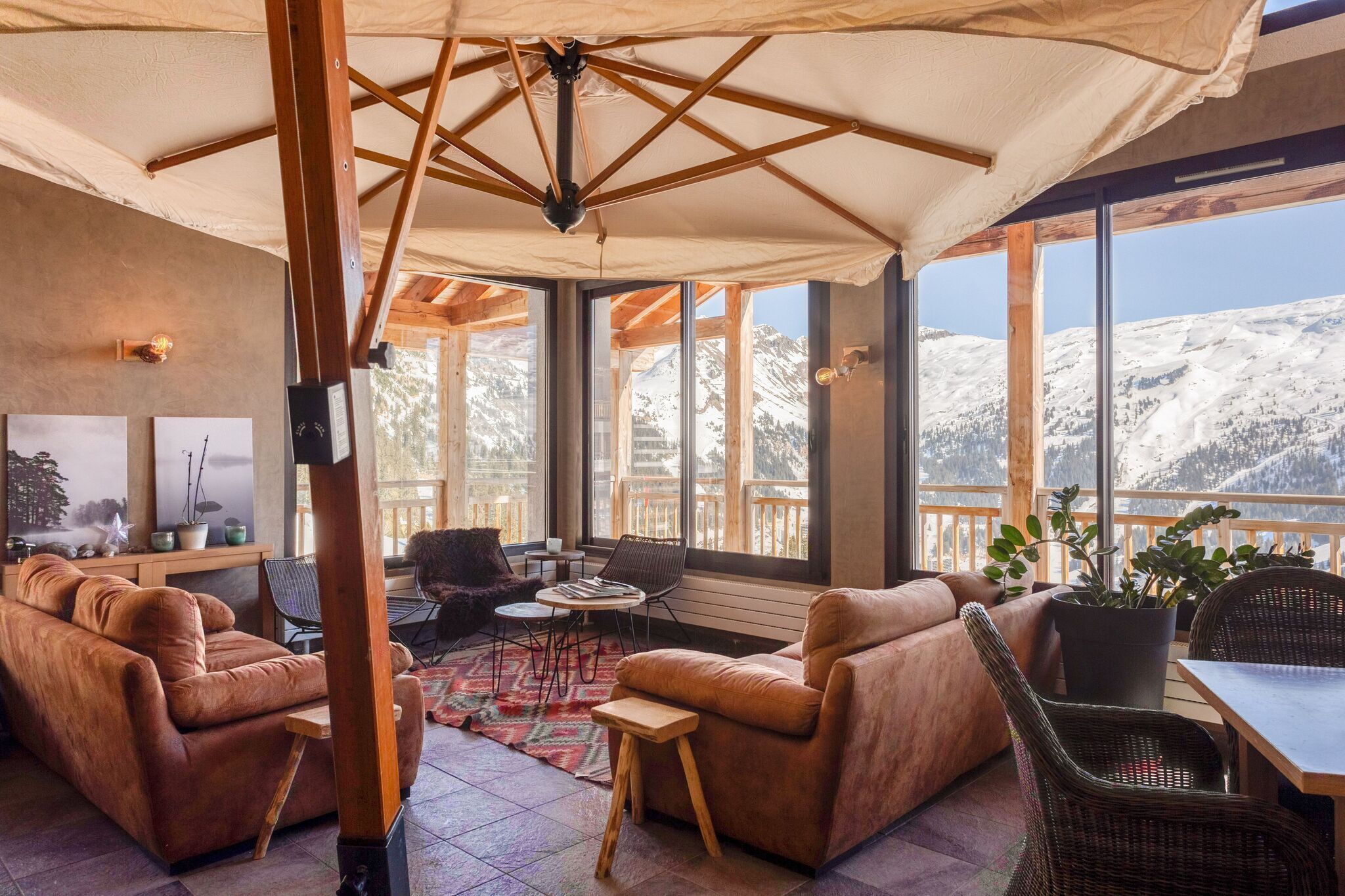 Un salon confortable doté d’une grande fenêtre donnant sur les montagnes, aménagé avec des canapés en cuir et des fauteuils en osier, ainsi qu’une table en bois.