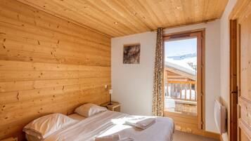 Une chambre à coucher aux murs lambrissés, avec un lit, une table de chevet, une lampe et une fenêtre donnant sur un paysage enneigé.