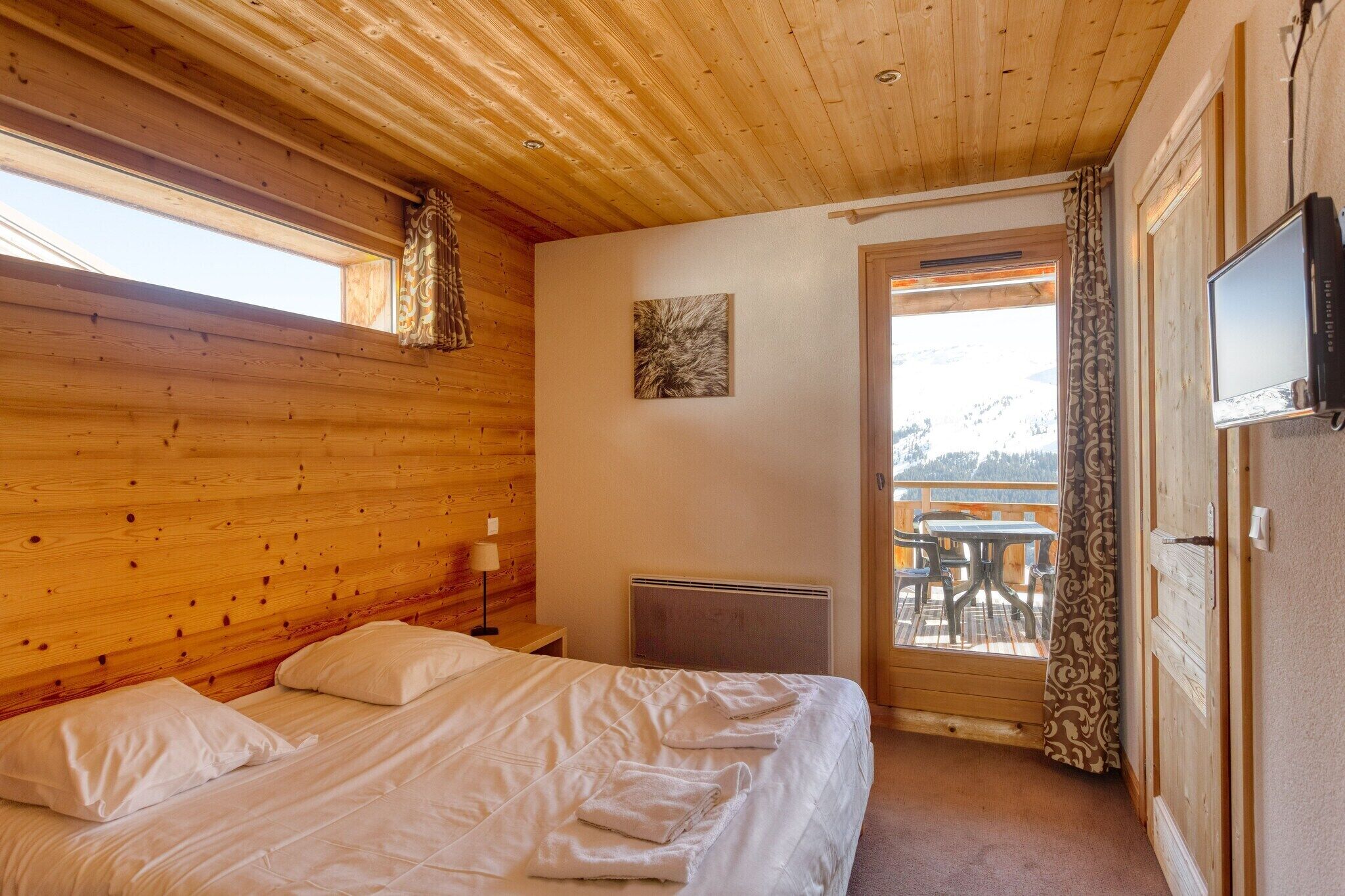 Une pièce aux murs lambrés, avec un lit, une table et des chaises à l’extérieur, et un téléviseur fixé au mur.