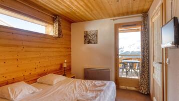 Une pièce aux murs lambrés, avec un lit, une table et des chaises à l’extérieur, et un téléviseur fixé au mur.
