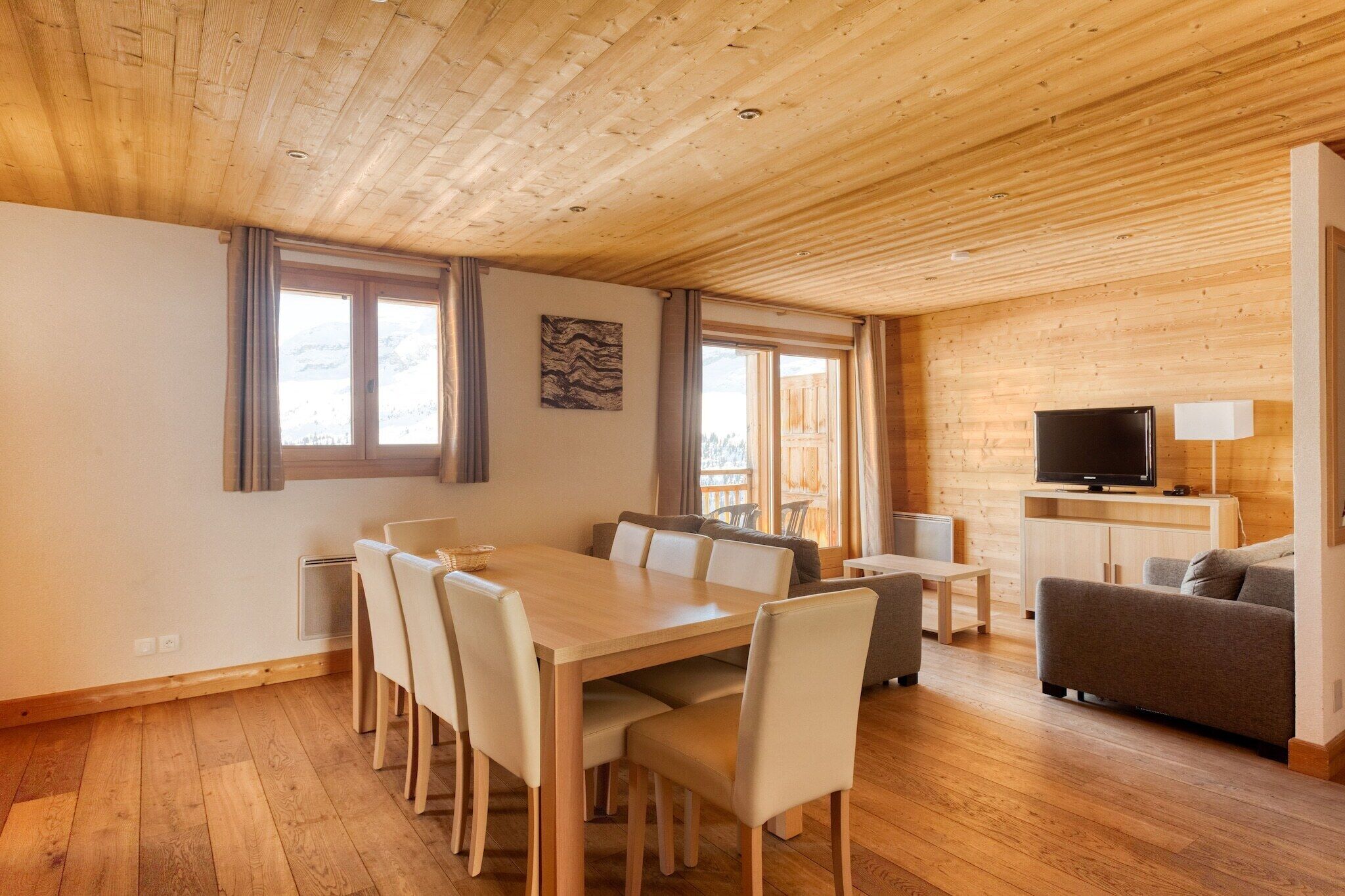 A wooden-paneled room with a dining table, chairs, a sofa, a TV, and a lamp.