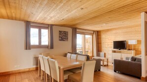 A wooden-paneled room with a dining table, chairs, a sofa, a TV, and a lamp. - Luxe Apartment w/ Ski (Arâches-La-Frasse)