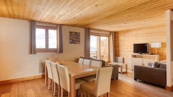 A wooden-paneled room with a dining table, chairs, a sofa, a TV, and a lamp.