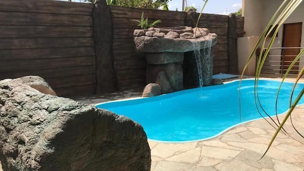 Una piscina con cascada, rodeada por un muro de piedra y una valla de madera.