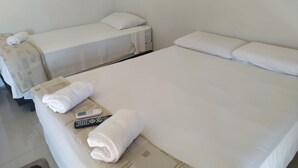 Habitación de hotel con dos camas individuales, una cama más grande y una mesita de noche con un control remoto y toallas.