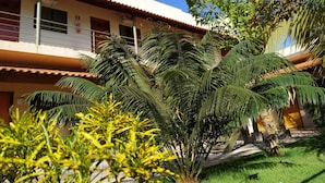 Un edificio con tejado de baldosas, balcón y jardín con palmeras y plantas florecientes amarillas.