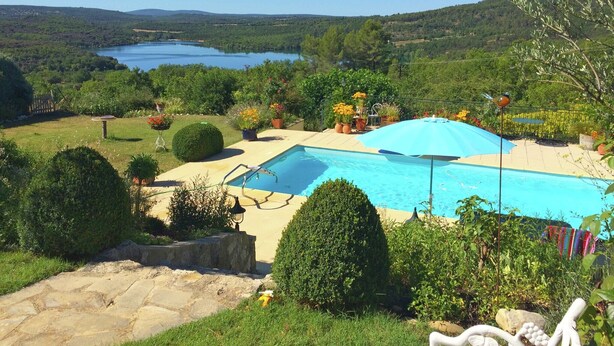 A swimming pool with a blue umbrella, surrounded by greenery and a view of a lake. - Verdon Views: Pool & Terrace (Montagnac Montpézat)