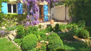 A garden with purple flowering vines, a patio with a chair, and a building with blue shutters. - Verdon Views: Pool & Terrace (Montagnac Montpézat)