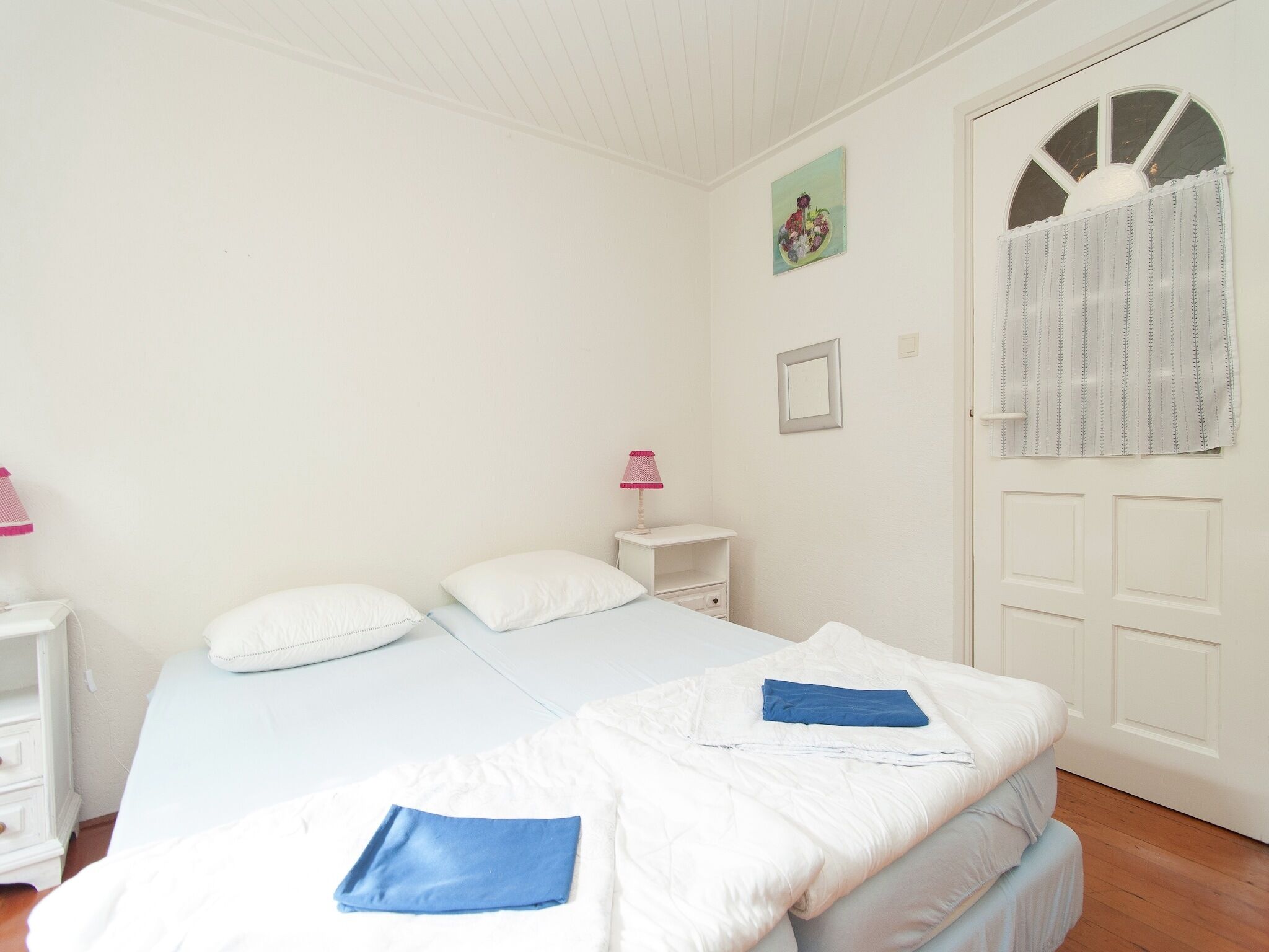 A bedroom with a bed, bedside tables, a nightstand, a window with curtains, and a door.
