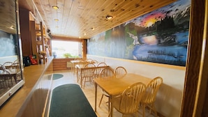 Een restaurant met houten tafels en stoelen, een muurschildering van een landschap en uitzicht op de omgeving.