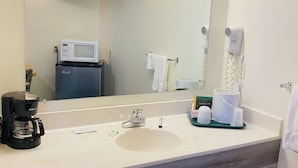 Een badkamer met een grote spiegel, een wastafel, een koffiezetapparaat, een haardroger en een magnetron.