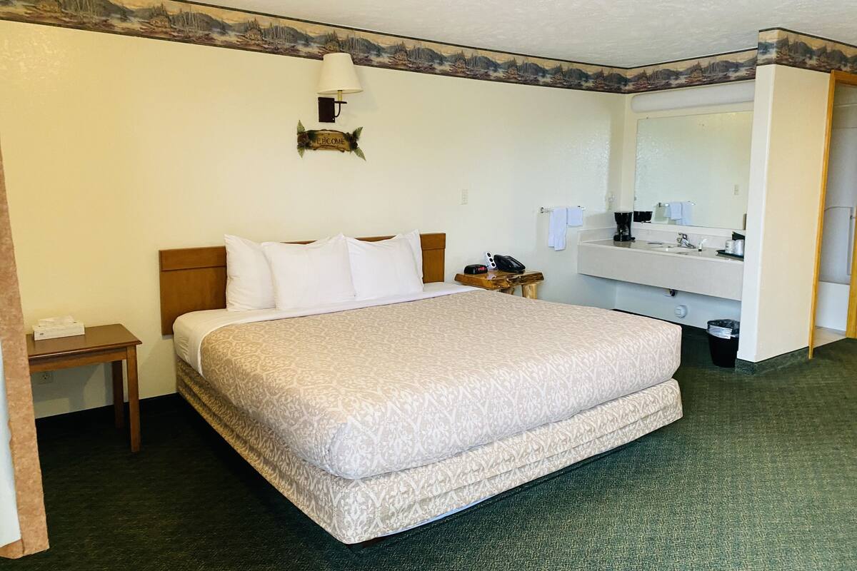 Une chambre d’hôtel avec un grand lit, une table de chevet, une lampe, un téléphone et une salle de bain équipée d’un lavabo et d’un miroir.
