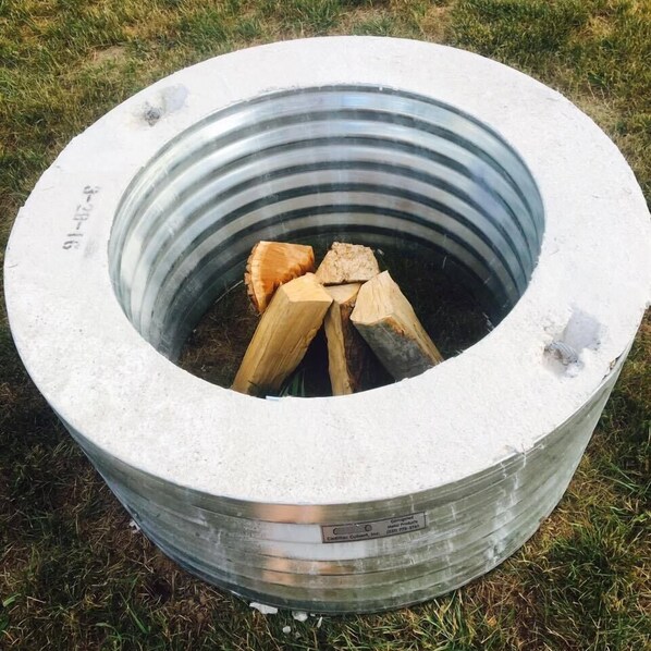 A metal fire pit with logs inside, placed on grass.