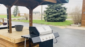 Een barbecue-opstelling buiten, met een grill en een houten tafel, onder een overdekt terras.