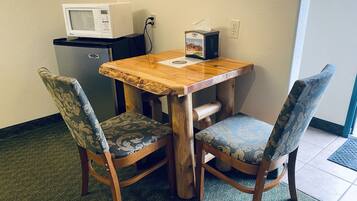 A small wooden table with two upholstered chairs, a microwave, and a tissue box on the table.