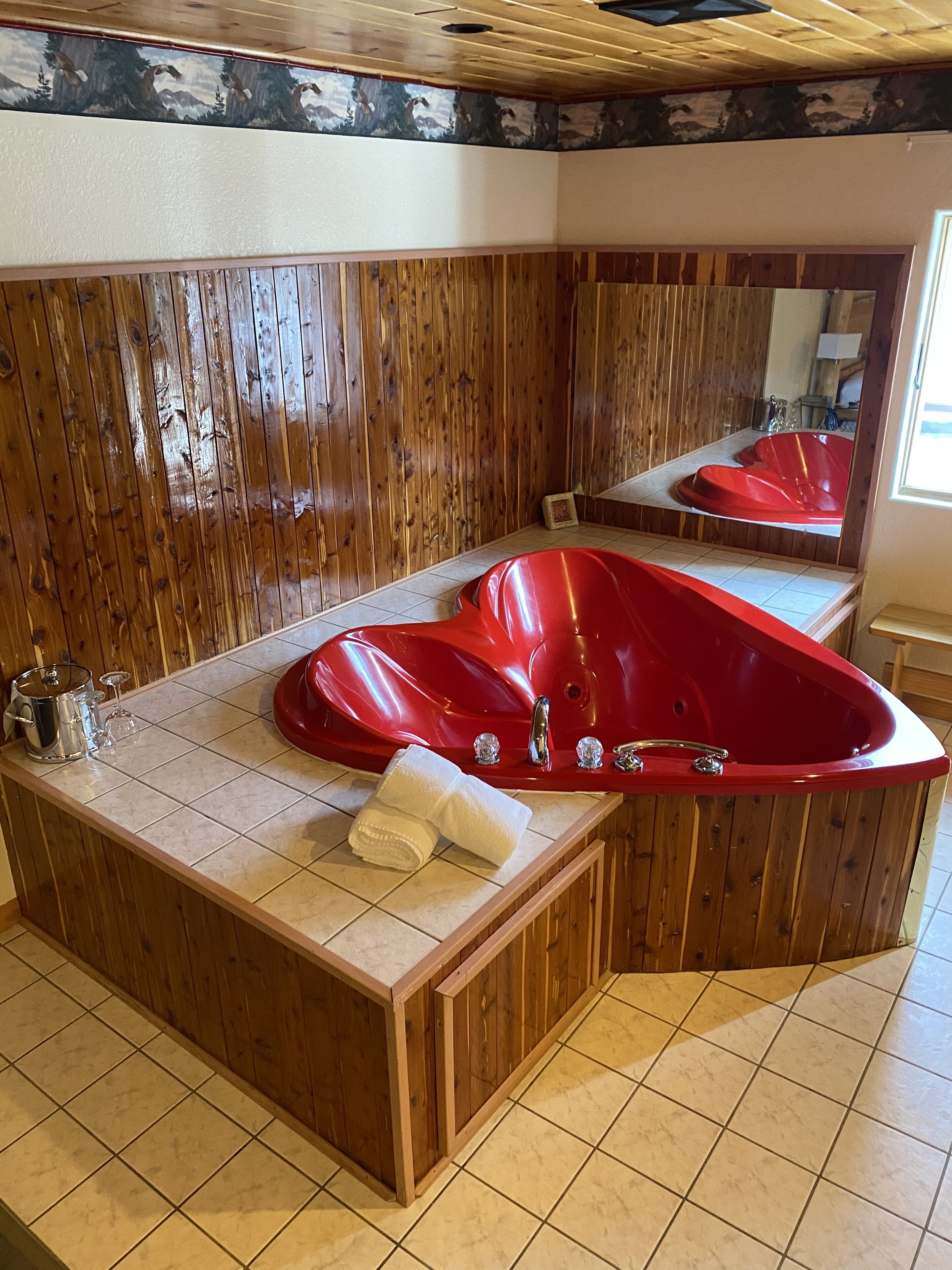 A bathroom with a wooden panel wall, a red bathtub, and a tiled floor.