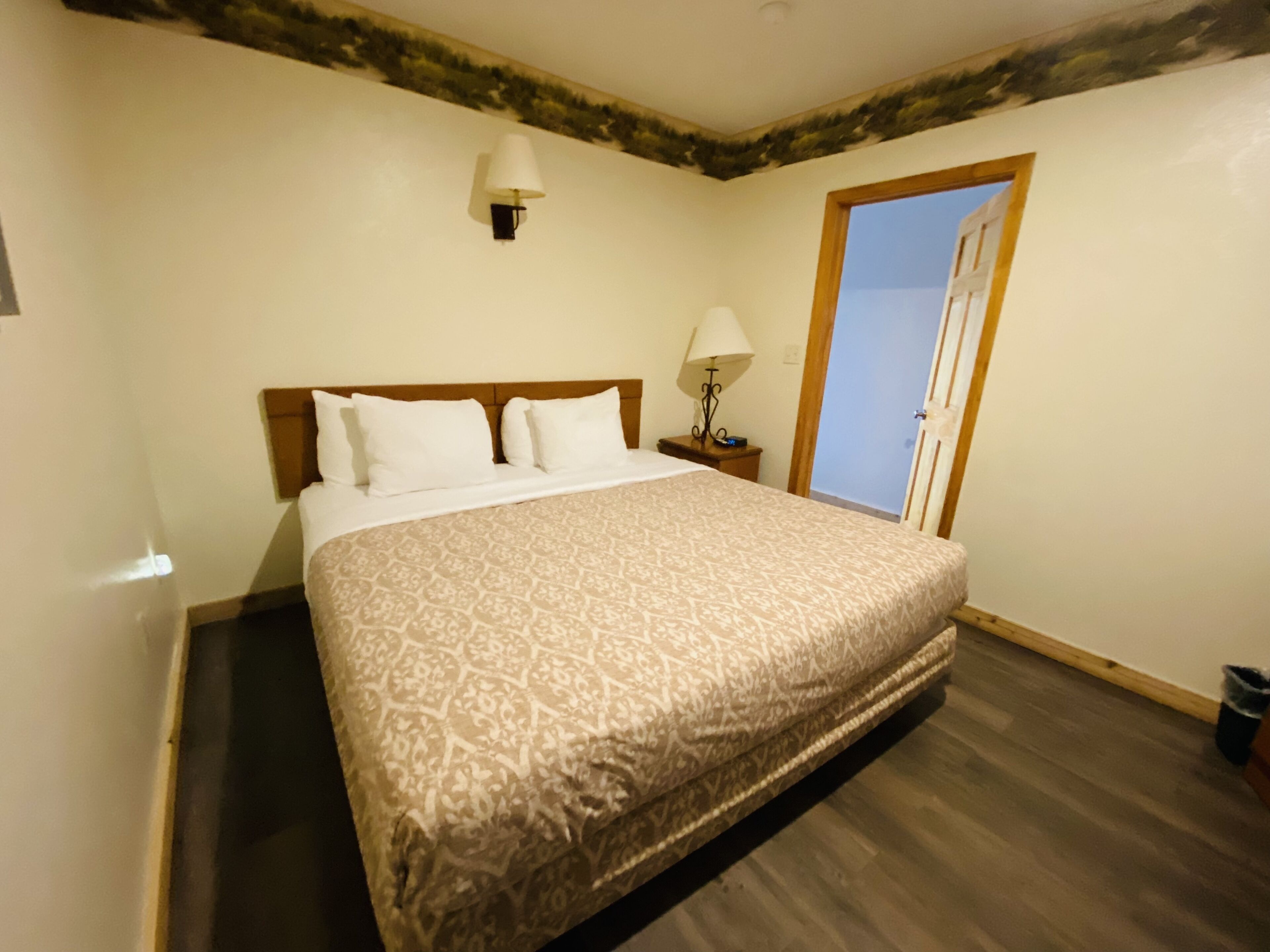 A bedroom with a large bed, a nightstand, a lamp, and a door leading to a balcony.
