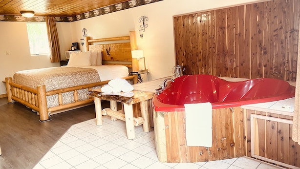 Een houten kamer met een bed, een rode badkuip en een kleine tafel.